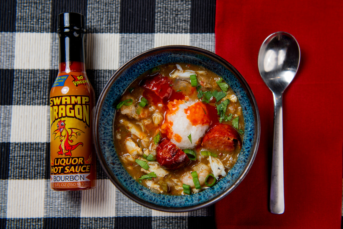 Bottle of Swamp Dragon Bourbon Hot Sauce next to a bowl of creole seafood and sausage gumbo