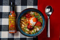 Bottle of Swamp Dragon Bourbon Hot Sauce next to a bowl of creole seafood and sausage gumbo