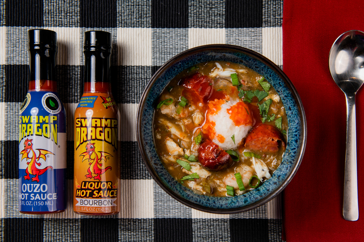 Bottles of Ouzo Hot Sauce and Bourbon Hot Sauce with a bowl of seafood and sausage gumbo