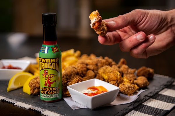Bottle of Swamp Dragon Rum Hot Sauce next to a hand dipping fried shrimp into a tartar sauce