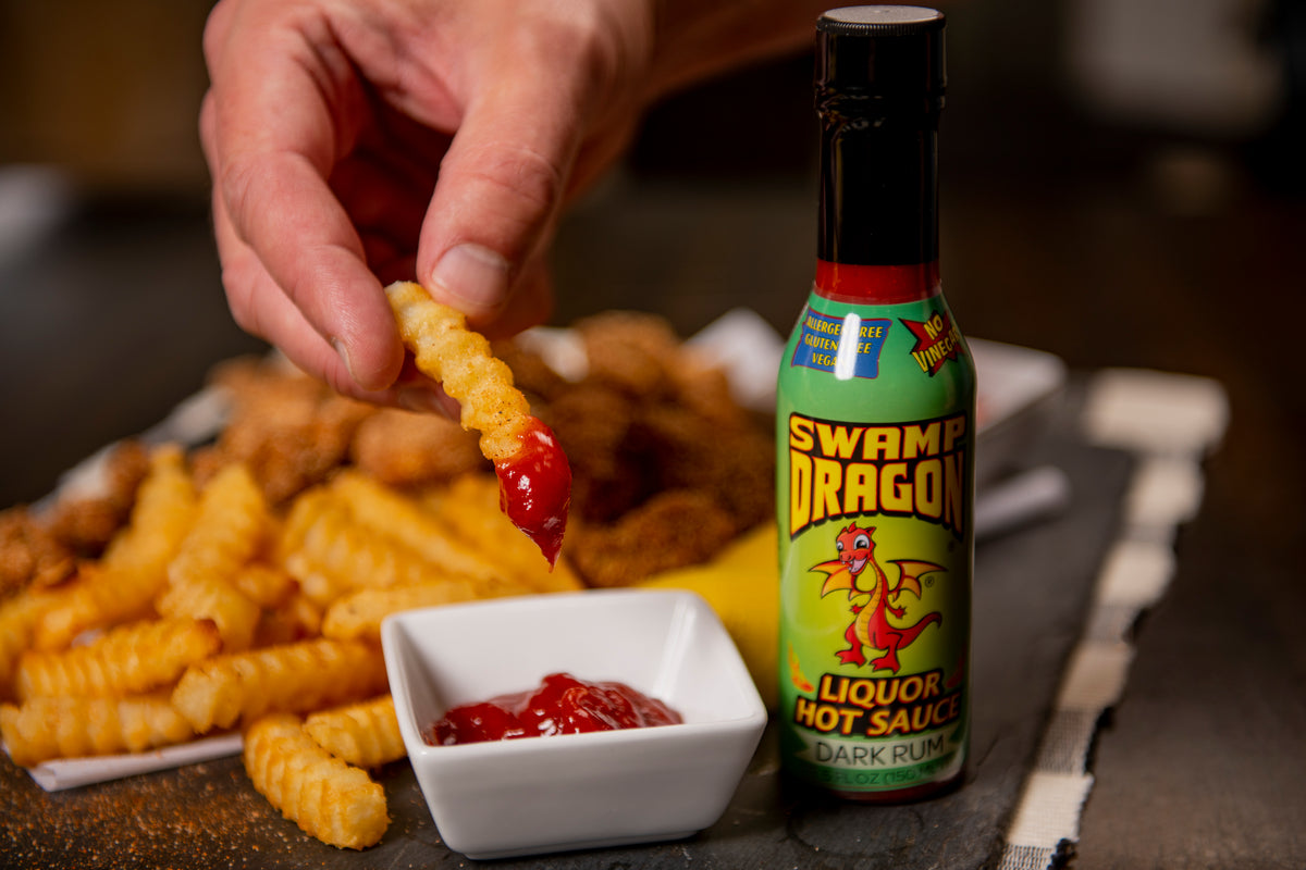 A hand dipping a french fry into ketchup spiced with Swamp Dragon Rum Hot Sauce 