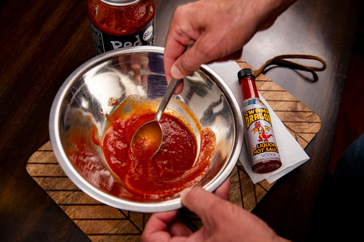 Hands stirring Swamp Dragon Vodka Hot Sauce into Italian tomato sauce in a stainless mixing bowl